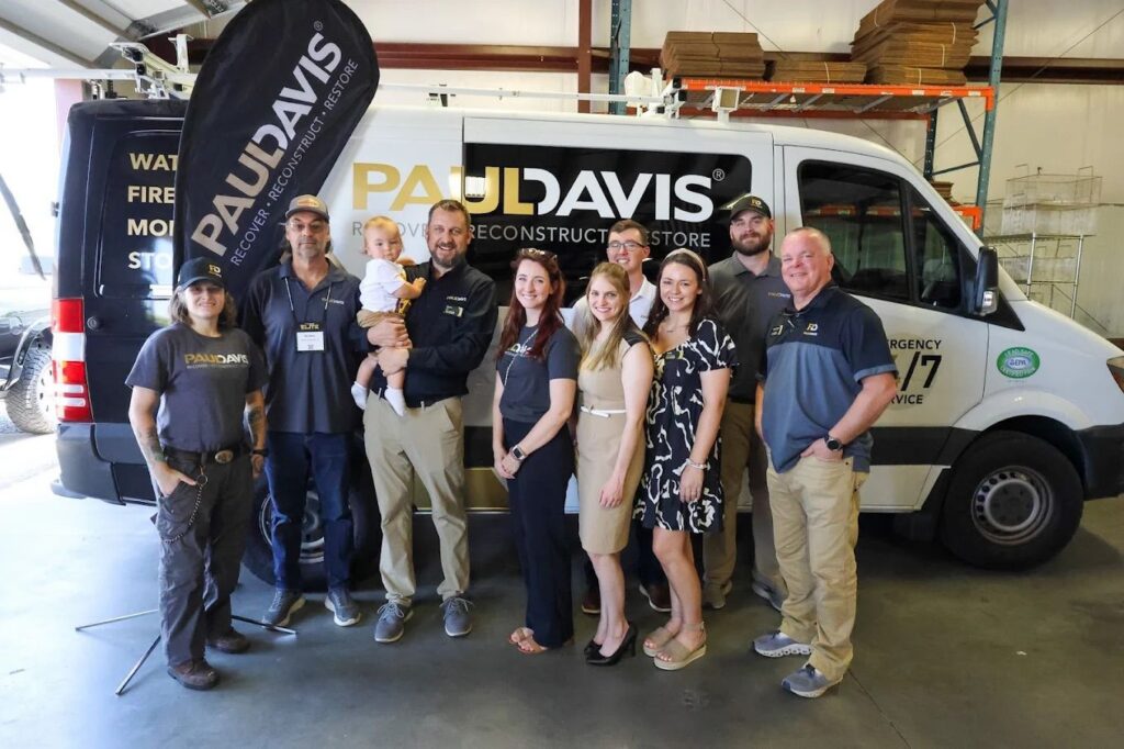 Paul Davis Restoration of Mobile team gathered in front of emergency restoration van inside warehouse, providing 24/7 water, fire, mold, and storm damage restoration services in Mobile, AL.